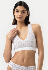 Spitzen-Bralette in Weiß mit tiefem V-Ausschnitt, strukturiertem Blumenmuster und breiten Spitzen-Trägern; kombiniert mit einem kontrastierenden weißen elastischen Band.