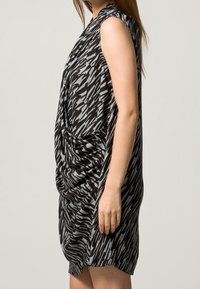 Ärmelloses Kleid in einem schwarz-grauen Zickzackmuster, mit drapierten Details vorne, gefertigt aus einem glatten Stoff.