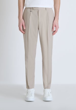 Pantaloni beige con vestibilità dritta, con due pieghe frontali e un dettaglio in clip metallico. Abbinati a sneakers bianche per un look pulito.