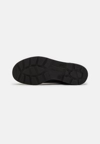 Suela de zapato de goma negra con una superficie texturizada, que presenta surcos pronunciados y un logo. El diseño incluye patrones rectangulares y circulares.