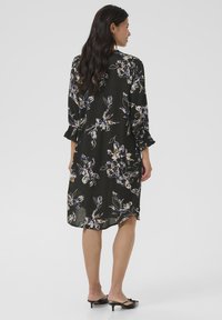 Rochie neagră cu flori, cu mâneci lungi, dintr-un material transparent și cu o croială lejeră. Are manșete volănașe și un model floral multicolor. Stil de lungime medie.