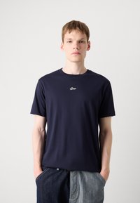 Tricou din bumbac de culoare albastru marin, cu guler rotund și un logo mic alb pe piept; cu mâneci scurte și o croială lejeră.