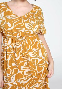 Żółta sukienka w kwiaty z białymi abstrakcyjnymi wzorami, krótkiem rękawem, dekoltem w serek i regulowanym sznurkiem w talii, zapewniająca luźny krój.