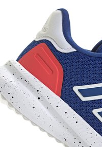 Blauer Sportschuh mit roten und weißen Akzenten. Obermaterial aus Mesh mit strukturiertem Muster, gepolsterte Sohle mit gesprenkeltem Design.