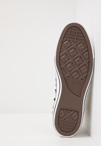 Hnědá gumová podrážka s texturovaným gripem, s bílým okrajem. Na podrážce se nachází logo "Converse All Star".