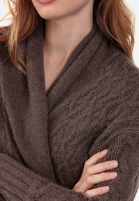 Cardigan marron en maille avec un motif texturé et un col châle. Le tissu semble doux avec des poignets côtelés et une coupe décontractée.