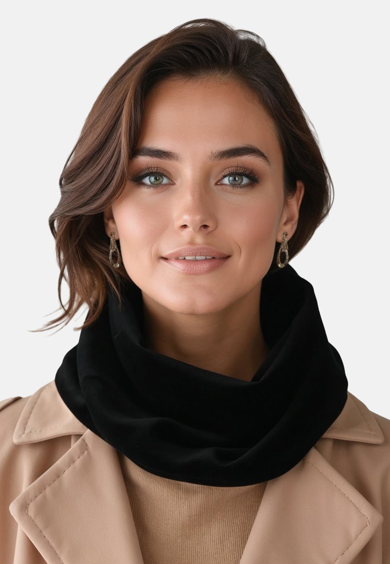 Mujer con cabello castaño hasta los hombros, que lleva pendientes dorados, una bufanda negra, un abrigo beige y una blusa marrón claro, mirando al frente.