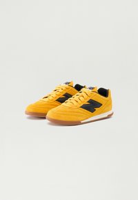 Yellow suede sneakers with black detailing, round laces, and gum rubber soles, featuring a distinctive logo on the tongue.