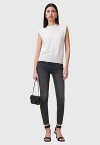 Top blanco sin mangas con dobladillo acanalado, combinado con jeans oscuros ajustados. Bolso negro con correa y sandalias negras de tacón. Diseño simple.