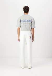 Grå kortermet t-skjorte med blå "ALLSAINTS" tekst på baksiden, kombinert med hvite bukser med to lommer og broderte detaljer.