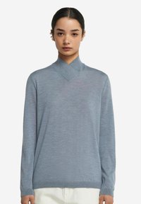 Jasnoniebieski sweter z dzianiny z krzyżowym kołnierzem i długimi rękawami. Gładka tekstura, lekko luźny krój i ściągacze przy mankietach.