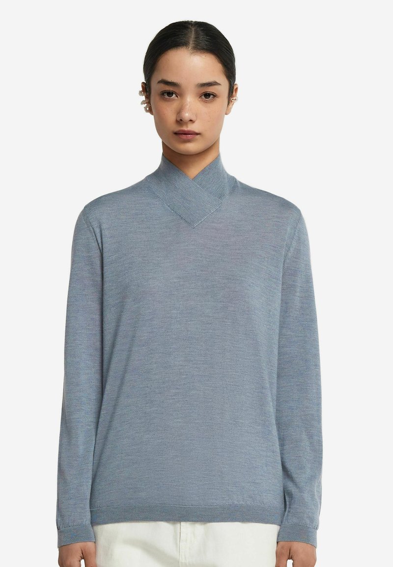 Jasnoniebieski sweter z dzianiny z krzyżowym kołnierzem i długimi rękawami. Gładka tekstura, lekko luźny krój i ściągacze przy mankietach.