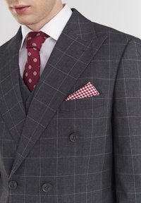 Szary marynarka w kratę z białymi liniami, zapinana na podwójne guziki, dwa guziki z przodu oraz czerwona, wzorzysta krawat w połączeniu z białą koszulą.