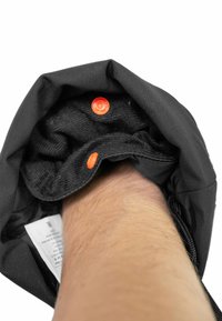 Schwarzer Stoff-Handgelenkschutz mit orangefarbenen Knopfdetails, ausgestattet mit einer weichen Innenseite und einem sichtbaren Pflegeetikett, das innen eingeklebt ist.