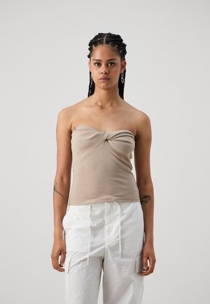 Haut beige côtelé sans bretelles avec un design frontal twisté. Porté avec un pantalon cargo blanc comportant un cordon de serrage, des poches latérales et une coupe décontractée.