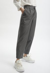 Szare spodnie w prążki z dopasowanym krojem, z wysokim stanem i bocznymi kieszeniami, stylizowane z białymi sneakersami.