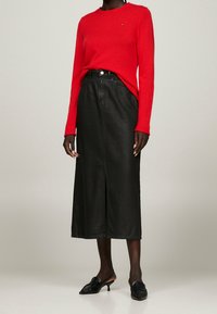 Roter Strickpullover mit langen Ärmeln und rundem Ausschnitt, kombiniert mit einem schwarzen Leder-Midirock mit einem vorderen Schlitz und klassischer Passform.