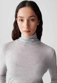 Hellgrauer Rollkragenpullover aus geripptem Stoff, mit einer taillierten Passform und weicher Textur. Nahtloser Halsausschnitt mit langen Ärmeln.