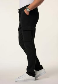 Zwarte cargo pants met zijzakken, elastische tailleband en trekkoord. Gecombineerd met witte sneakers, wat een ontspannen pasvorm laat zien.