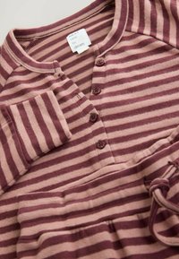 Pruhovaná látka v burgundskej a ružovej farbe, s okrúhlym výstrihom, gombíkovou légou a dlhými rukávmi s detailom náprsnej vrecka.