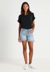 Black short-sleeve top paired with light blue denim shorts featuring a button-up front, rolled hem, and side pockets. White sneakers complete the look.
