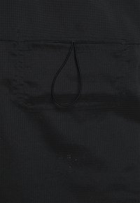 Černá textilie s texturovaným vzorem a elastickým stahovacím provázkem. Obsahuje plochou kapsu, viditelné švy a hladký povrch.