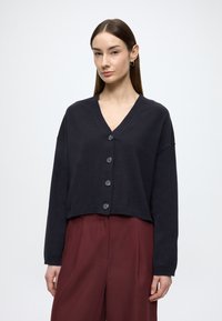 Cardigã curto azul escuro com decote em V, apresenta seis botões cinzentos na frente e mangas largas. Textura suave, design minimalista.