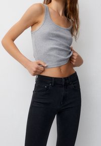 Débardeur gris côtelé avec encolure dégagée, associé à un jean noir taille haute. Le débardeur présente une coupe ajustée et une longueur raccourcie.