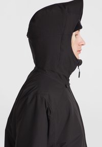 Chaqueta negra con capucha y cuello alto, que cuenta con cierre de cremallera y bolsillos laterales. Textura suave con un diseño ajustado.