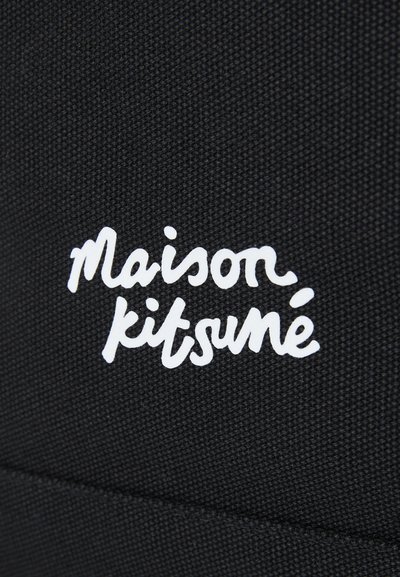 Un tissu noir texturé présente un logo en cursive blanc "Maison Kitsuné" affiché de manière proéminente.