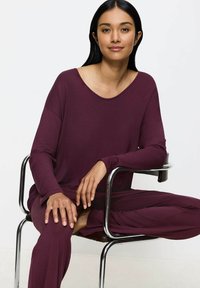 Conjunto de ropa de estar en burdeos que incluye una camiseta larga de manga suelta con un escote amplio y pantalones de corte relajado. Tejido suave y diseño sencillo.