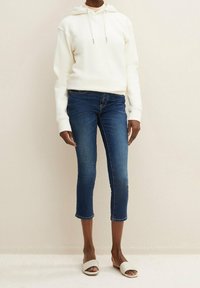 Vit hoodie med snörning, i kombination med mörkblå korta jeans och öppna vita sandaler. Slät tyg och avslappnad passform.