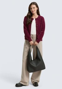 Bordeauxroter Strickcardigan mit rundem Ausschnitt und Knöpfen; kombiniert mit weißem Oberteil, beigen weiten Hosen und einer großen schwarzen Hobo-Tasche.