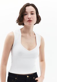 Top aderente bianco con scollatura a V profonda e spalline larghe, realizzato in un tessuto morbido, abbinato a jeans in denim scuri.
