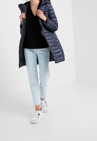 Laivaston sininen toppatakki hupulla, musta V-aukkoinen villapaita, vaaleansiniset farkut ja valkoiset lenkkarit, joissa on punaisia ja sinisiä yksityiskohtia.