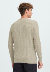 Heled beige kudumüts, millel on vertikaalne soonik, ümar kaelus ja soonikkoes mansetid. Pehme tekstuur, keskmise pikkusega ja keha lähedane siluett.