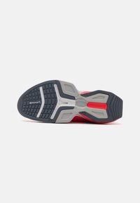 Semelle de chaussure de sport avec une semelle en caoutchouc texturé gris et noir, ornée d'accents rouges et de marquages, conçue pour l'adhérence et la flexibilité.