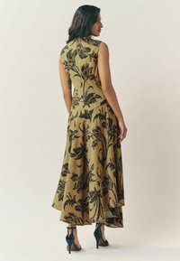 Rochie fără mâneci, cu un design cu motive florale negre pe fundal kaki, cu fustă evazată și lungime până la gleznă.