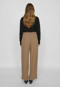 Bruna vida-byxor med elastisk midjeband, tillverkade av ett slätt tyg. Matchas med en svart topp med broderade detaljer på ärmarna.