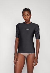 Čierny krátky rukáv rash guard vyrobený z hladkej, elastickej tkaniny. Obsahuje biele logo na hrudníku a vysoký golier.