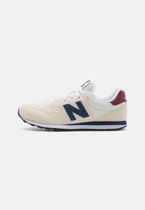 Scarpe sportive beige realizzate con materiali in rete e camoscio. Presentano un logo "N" blu navy, lacci bianchi e un accento bordeaux sul tallone. Suola in gomma nera.