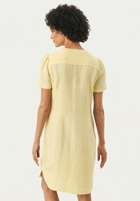 Kurzes gelbes Leinenkleid mit kurzen Puffärmeln, einer Rückenpasse und seitlichen Schlitzen. Es hat einen strukturierten Stoff und eine lockere Passform.