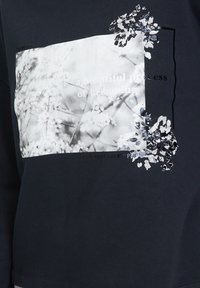Tissu noir à motif floral blanc flou avec des détails de fleurs noires, comportant le texte « un beau processus de devenir ».
