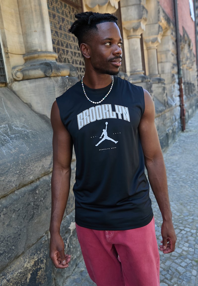 Čierne bezrukávové tričko s bielym nápisom "BROOKLYN" a siluetou loga. V páre s ružovými nohavicami. Hladká tkanina, voľný strih.