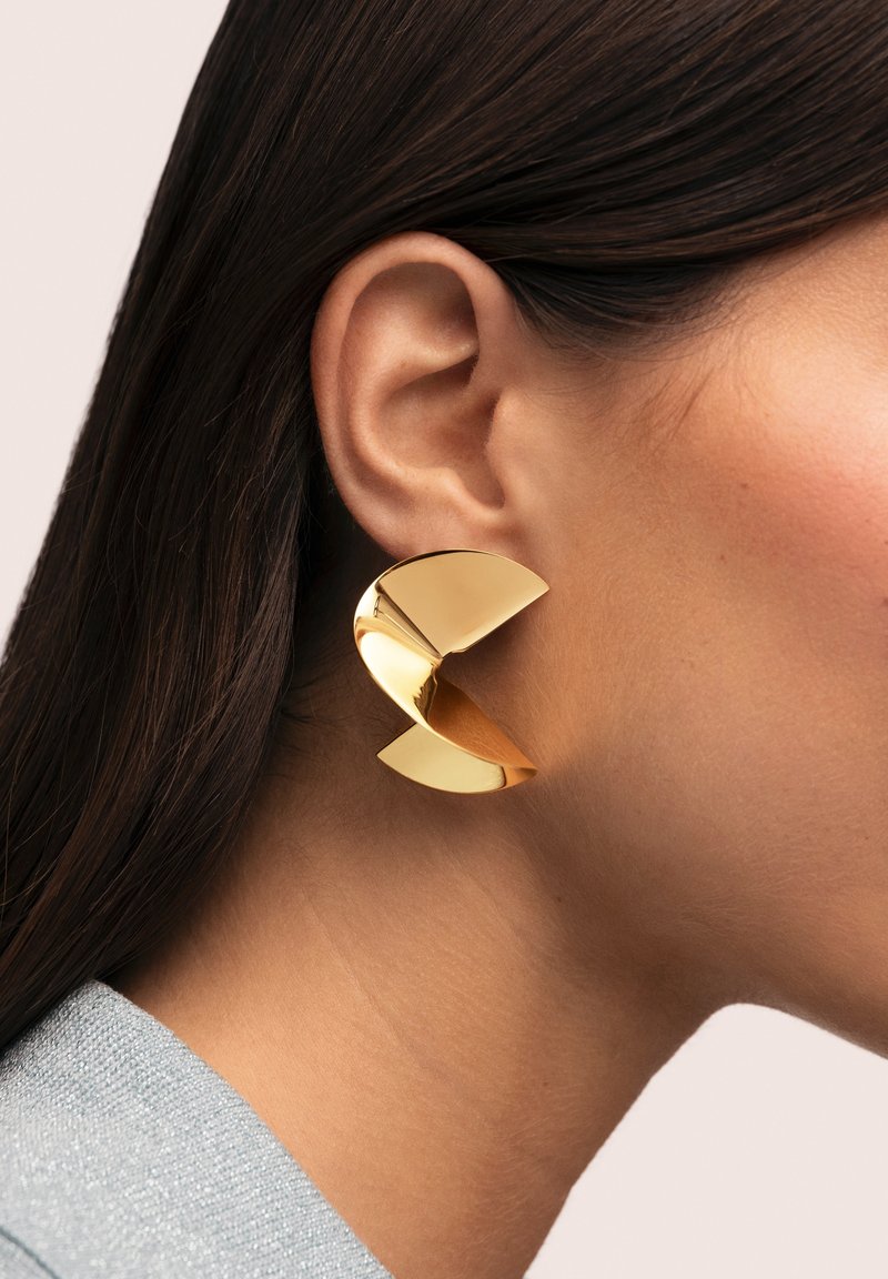 Pendiente llamativo de color dorado con un diseño escultórico de forma curva y geométrica y acabado brillante.