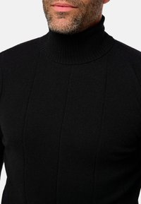 Schwarzer Rollkragenpullover aus Strickstoff, mit gerippter Textur und vertikalen Nahtdetails. Nahaufnahme von Nacken und Schultern.