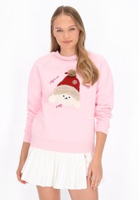 Sudadera rosa con un perro de peluche que lleva un gorro rojo con pompón, con texto bordado y una textura suave. Combinada con una falda blanca plisada.