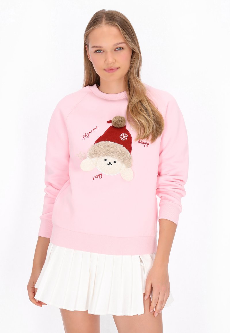 Sudadera rosa con un perro de peluche que lleva un gorro rojo con pompón, con texto bordado y una textura suave. Combinada con una falda blanca plisada.