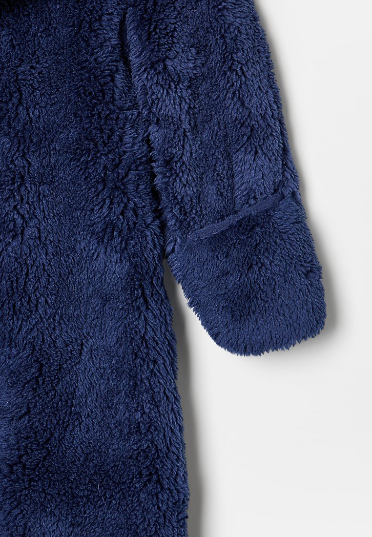 Mörkblå fleecejacka med en mjuk, texturerad yta; har en rundad, manchetterad ärm och en avslappnad passform.