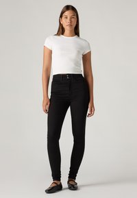 White ribbed short-sleeve top paired with high-waisted black skinny jeans, accented by a button closure and black flats.